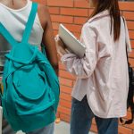 students walking outdoors carrying backpacks and a laptop, back to school scene