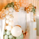 a professional-looking sage green, cream, and gold balloon arch installation