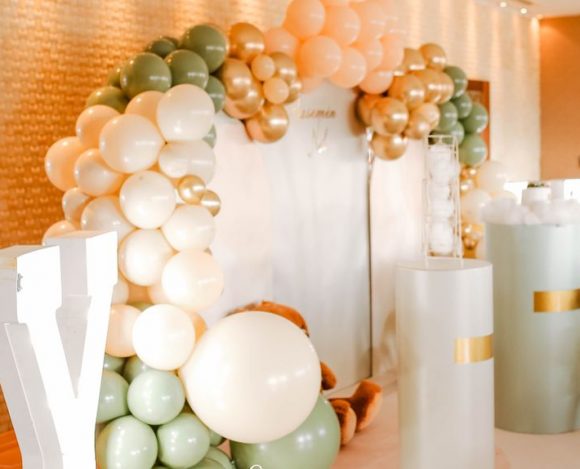 a professional-looking sage green, cream, and gold balloon arch installation