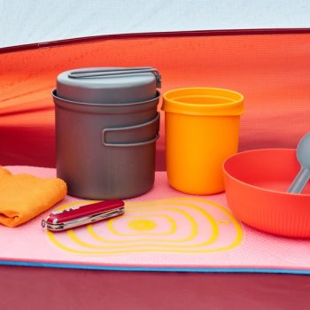 colorful camping cookware, multitool, and sleep pad arranged inside a tent