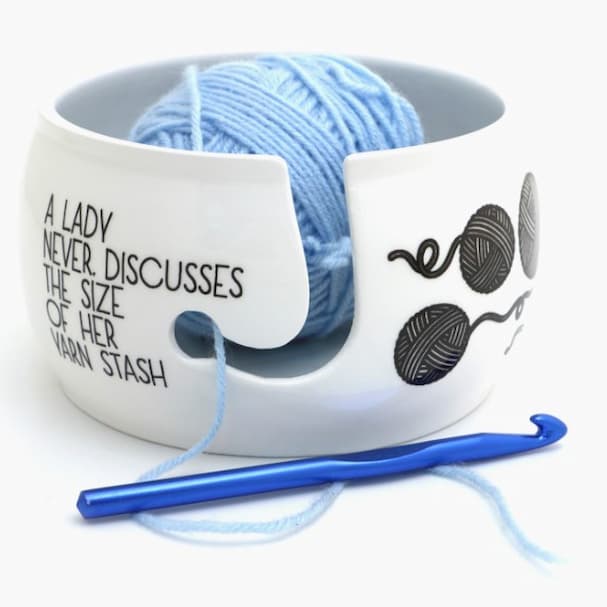Ceramic yarn bowl with yarn ball inside and crochet hook resting on top product photo
