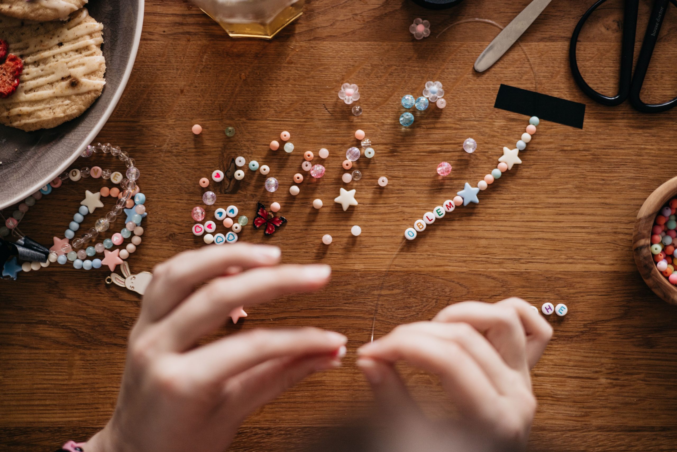 Hands stringing colorful clay beads and star beads for a friendship bracelet