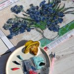 an in-progress diamond painting canvas of blue flowers with diamond bags and a drill pen on a wooden table