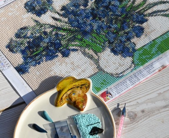 an in-progress diamond painting canvas of blue flowers with diamond bags and a drill pen on a wooden table