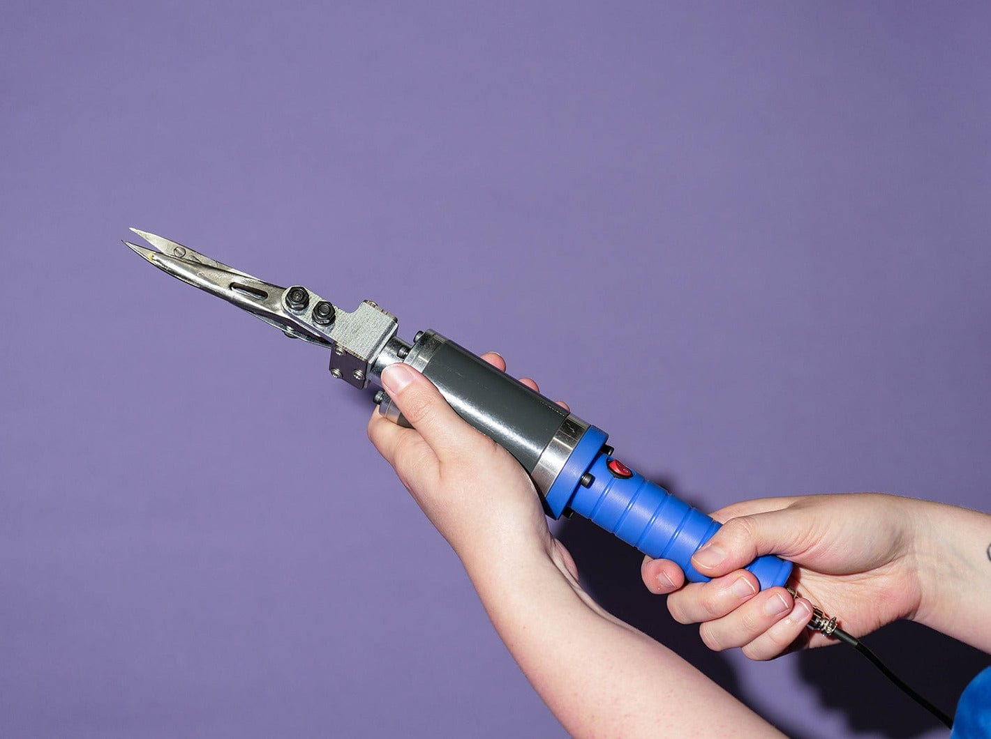 Electric rug carving scissors held in hands, sculpting detail into a tufted rug