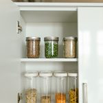 an organized white kitchen cabinet with mason jars and clear airtight containers of pantry staples