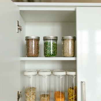 an organized white kitchen cabinet with mason jars and clear airtight containers of pantry staples