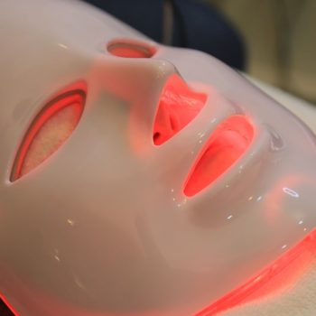 a white LED face mask glowing with red light therapy in use