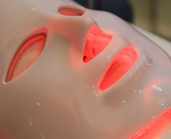 a white LED face mask glowing with red light therapy in use