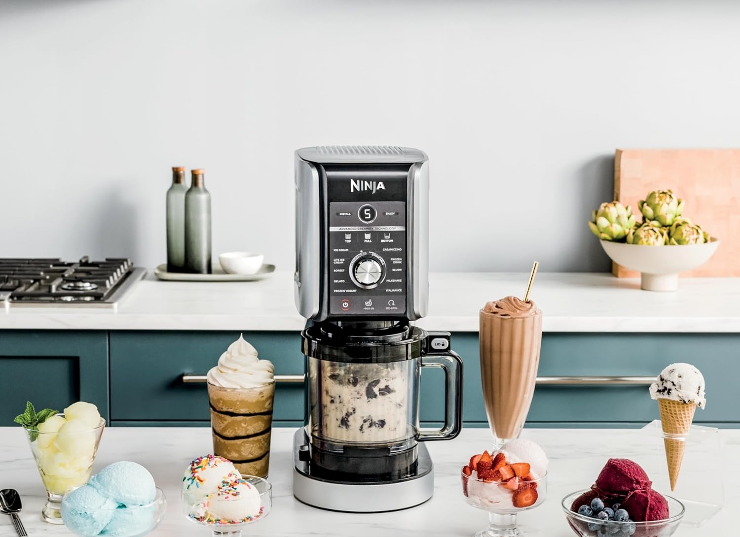 Ninja CREAMi XL Deluxe ice cream maker on a kitchen counter surrounded by ice cream, milkshakes, and sorbet