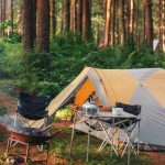 Cozy campsite scene with tent, camp chairs, fire pit, and a kettle with mugs on a table, best camping gifts