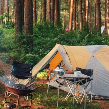 Cozy campsite scene with tent, camp chairs, fire pit, and a kettle with mugs on a table, best camping gifts