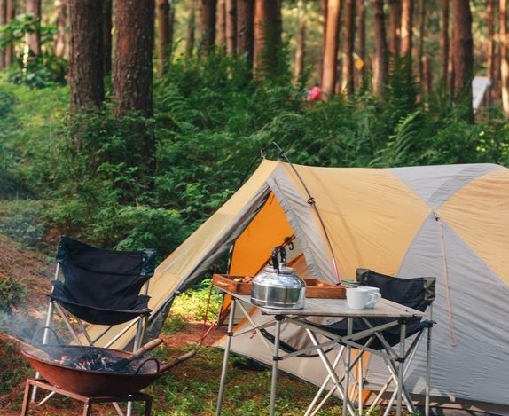 Cozy campsite scene with tent, camp chairs, fire pit, and a kettle with mugs on a table, best camping gifts