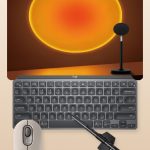 Collage of a desk setup with a sunset projection lamp, minimalist keyboard, mouse, and monitor light bar on a warm cream background