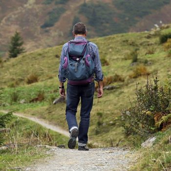 top-10-rucking-essentials-hero Hiker walking a mountain trail carrying a weighted backpack, best rucking gear