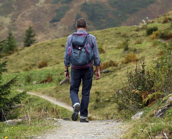 Hiker walking a mountain trail carrying a weighted backpack, best rucking gear