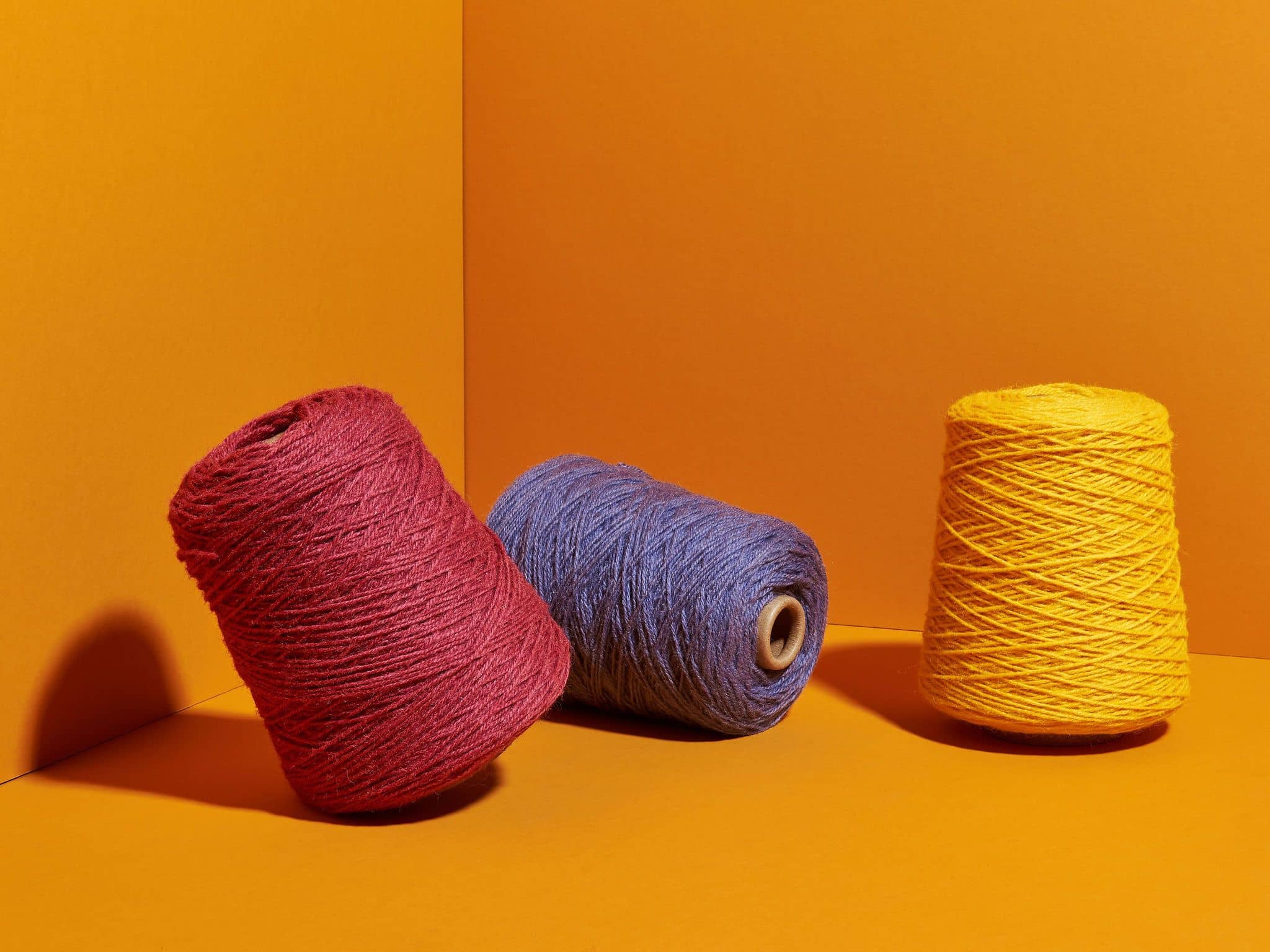Colorful yarn cones for rug tufting in red, purple, and yellow