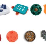 A clean two-row lineup of real dog enrichment toys on white, each grounded on a shared baseline: a Nina Ottosson Dog Casino puzzle, TRIXIE Activity Flip Board, Omega Paw Tricky Treat Ball, West Paw Toppl, KONG Wobbler, a treat ball, Outward Hound Fun Feeder Slo Bowl, and a LickiMat Tuff Soother 4-pack
