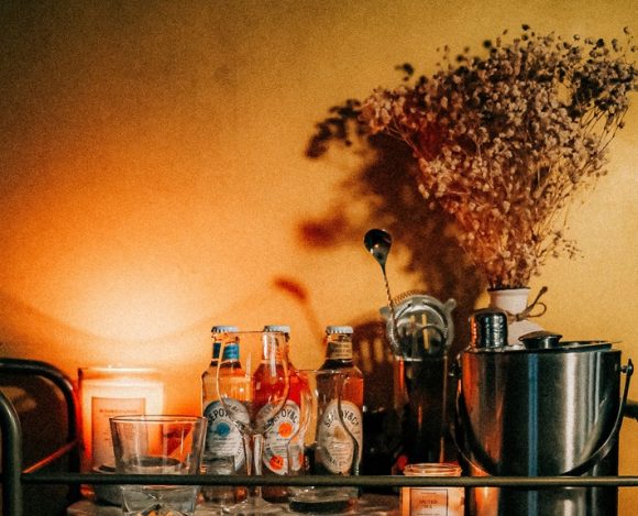Moody home bar cart styled with bottles, a cocktail shaker, candles, and dried flowers
