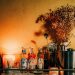 Moody home bar cart styled with bottles, a cocktail shaker, candles, and dried flowers