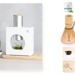 The Cuzen Matcha Maker dispensing fresh matcha into a glass on the left, with a Jade Leaf ceremonial matcha tin, a bamboo matcha whisk set, a black ceramic chawan bowl, and a stainless steel matcha sifter arranged on the right