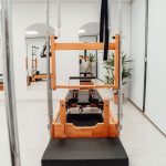 Wooden Pilates reformer and tower combo machine in a bright modern studio, pilates essentials