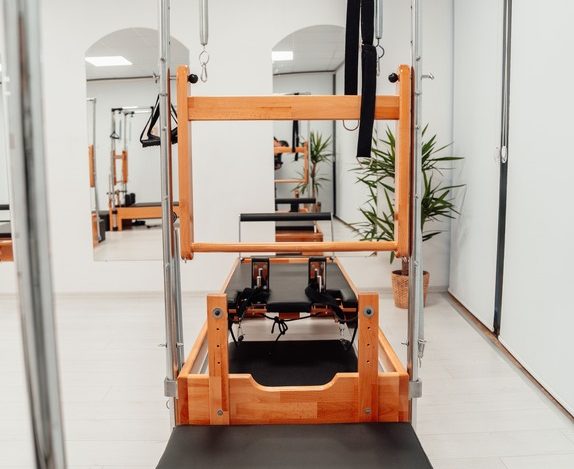 Wooden Pilates reformer and tower combo machine in a bright modern studio, pilates essentials