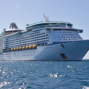 A large white cruise ship, Explorer of the Seas, sailing on clear blue ocean water under a bright blue sky