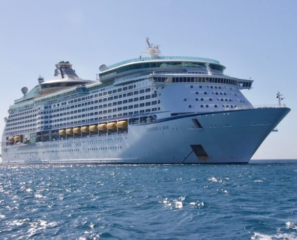 A large white cruise ship, Explorer of the Seas, sailing on clear blue ocean water under a bright blue sky
