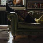 A person relaxing on a green couch reading a physical book with a stack of books nearby, choosing reading over screen time