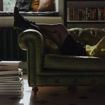 A person relaxing on a green couch reading a physical book with a stack of books nearby, choosing reading over screen time